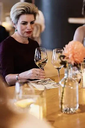 Woman holding wine glass at elegant event table with flowers and candles