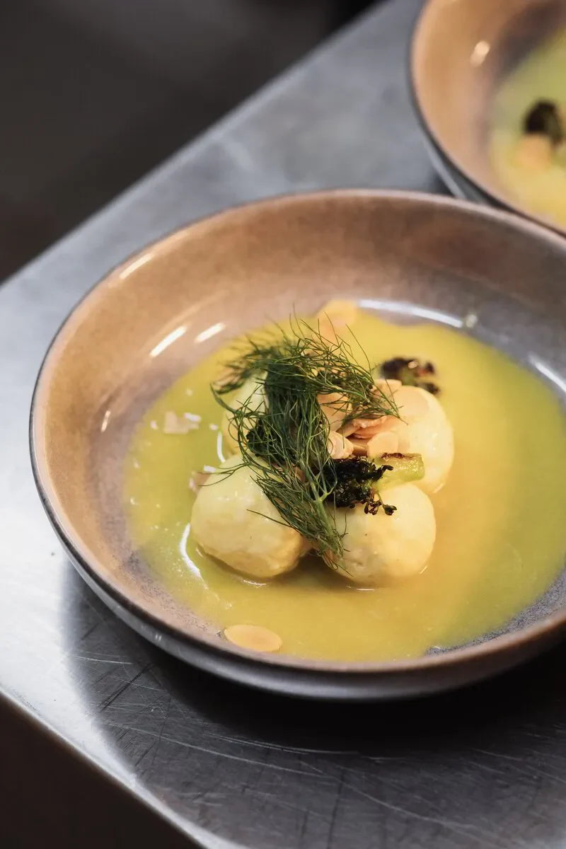 Gourmet dish with potato dumplings, yellow sauce, herbs and sliced almonds in a ceramic bowl