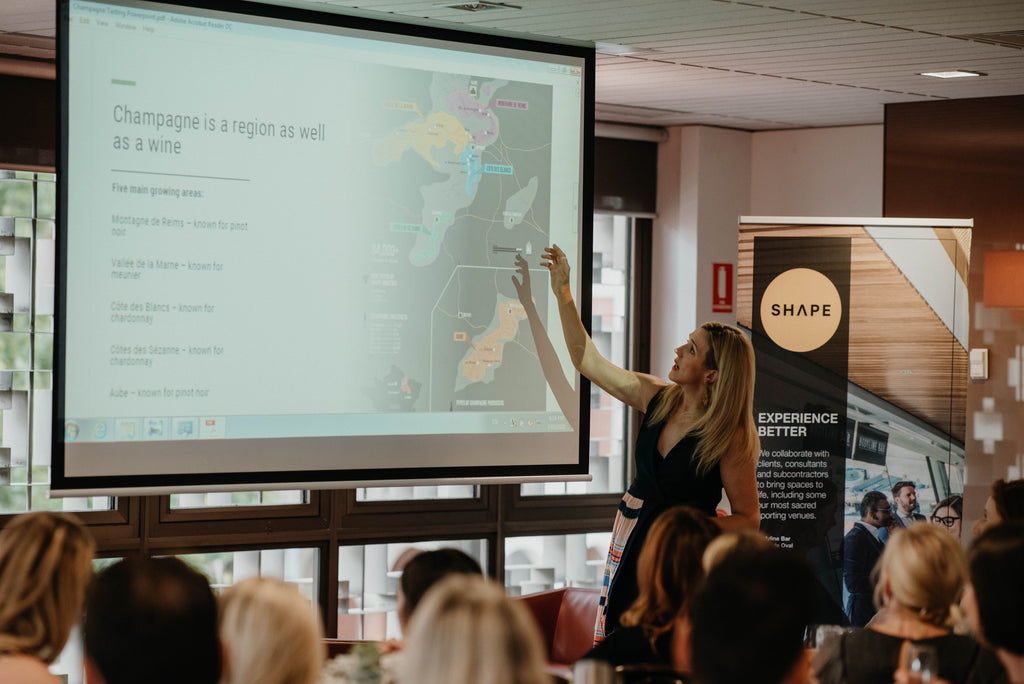 Woman leading a Champagne Foundations Course presentation with map and text projected in a bright modern room