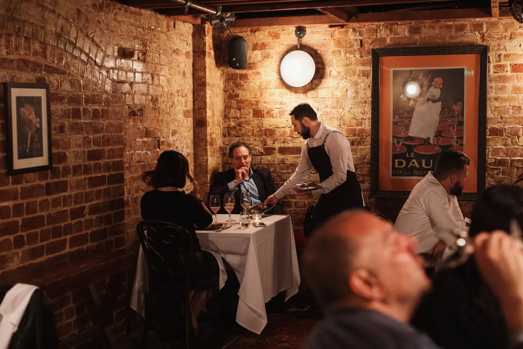 Cozy brick-walled restaurant with waiter serving couple at candle-lit table, warm ambiance