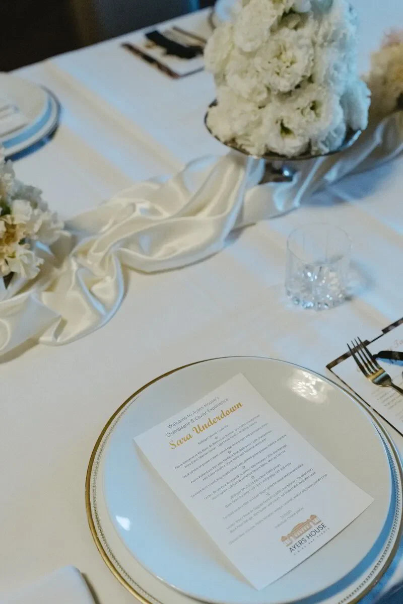 Elegant wedding table setting with white flowers, gold-rimmed plate, and printed menu card