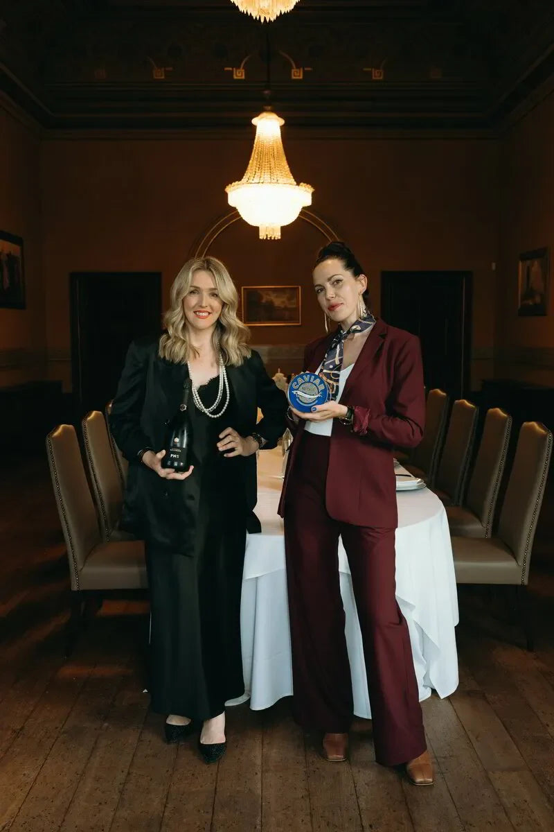 Two women in elegant suits holding champagne and caviar in a formal dining room