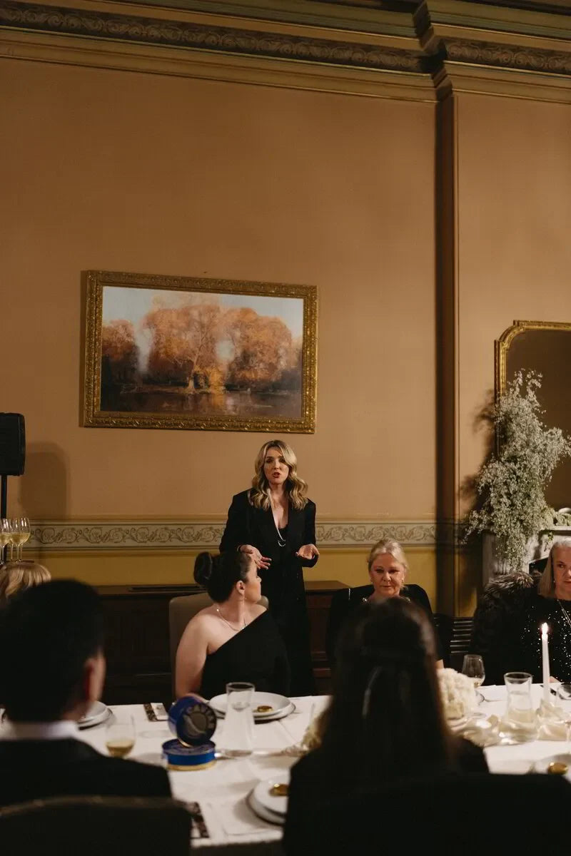 Elegant dinner party with a woman standing and speaking, formal dining room, art on wall