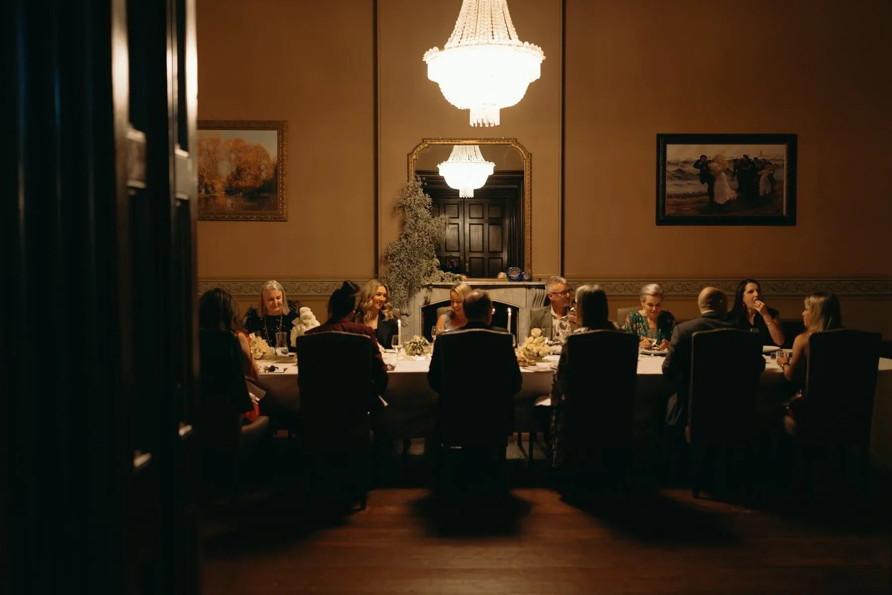 Elegant dinner party with guests seated around a long table under chandelier lighting.