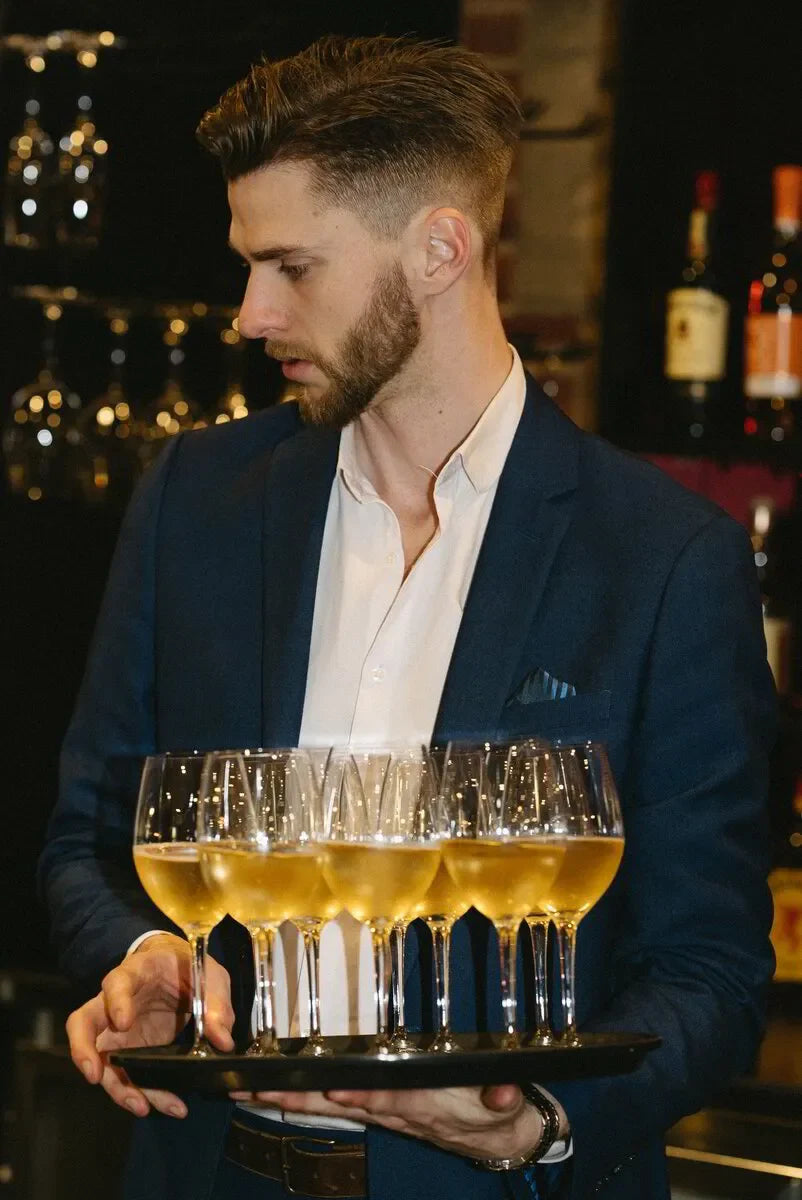 Waiter in blue suit serving tray of champagne glasses at upscale bar