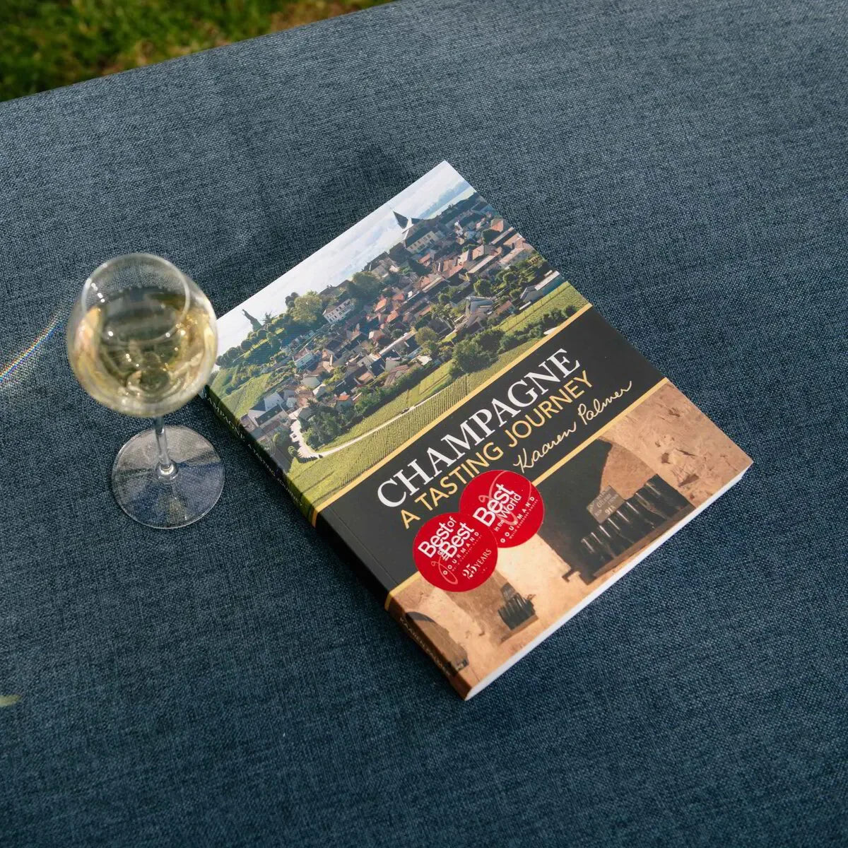 Champagne A Tasting Journey book with wine glass on blue fabric surface outdoors