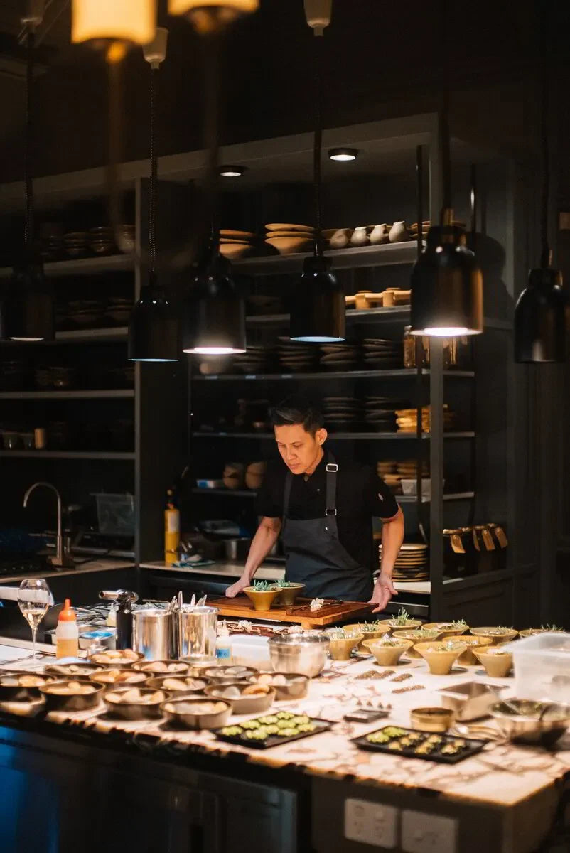 Chef in modern restaurant kitchen plating food under warm hanging lights