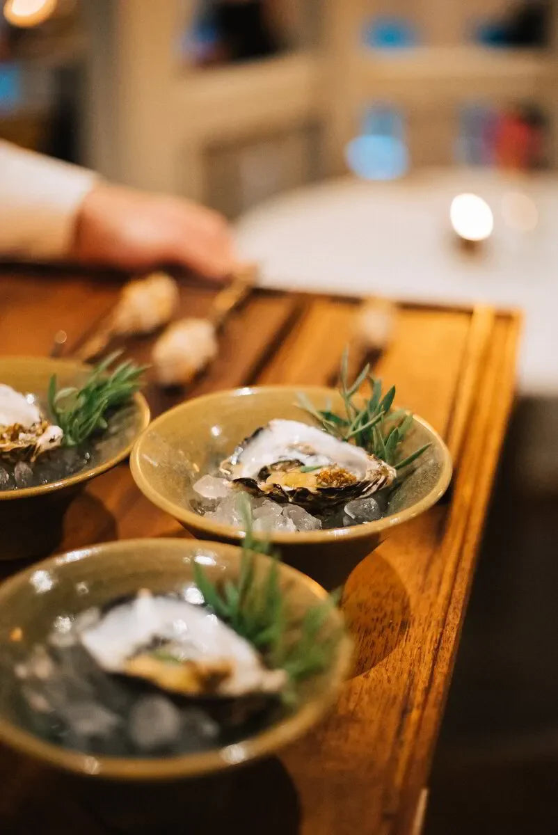 Fresh oysters on ice in ceramic bowls with herbs on a wooden tray, fine dining restaurant