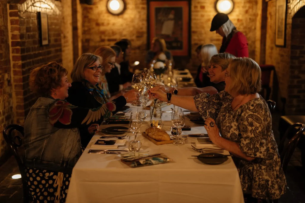 Group of women toasting wine at a cozy restaurant table with brick walls and warm lighting