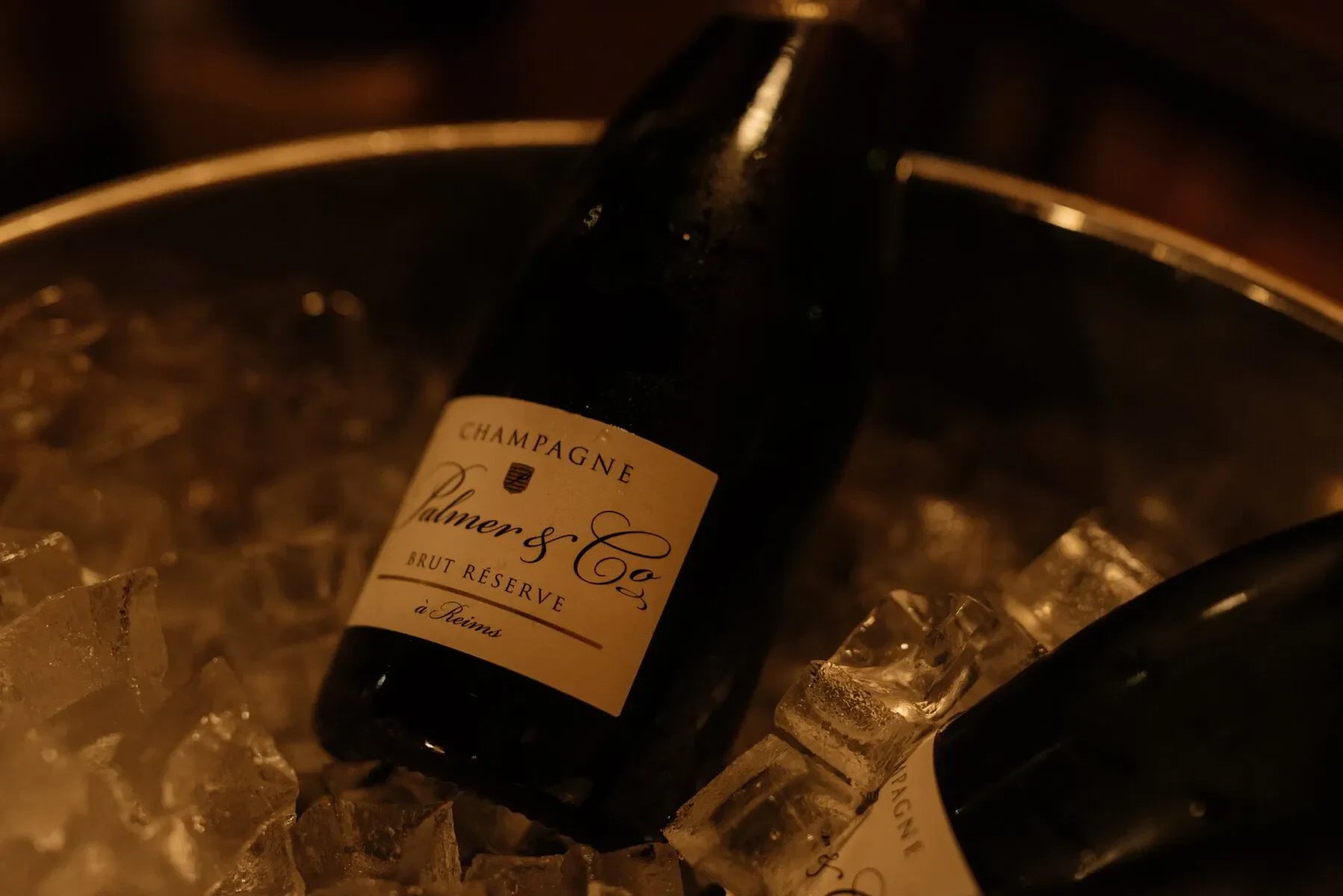 Palmer & Co Brut Reserve champagne bottle on ice in a metal bucket, dim lighting
