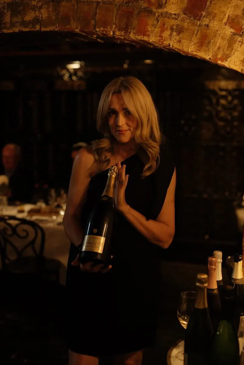 Woman in black dress holding champagne bottle in elegant wine cellar setting