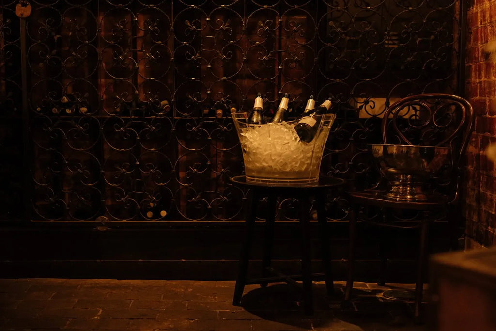 Champagne bottles in ice bucket on stool in dimly lit wine cellar with wrought iron gate