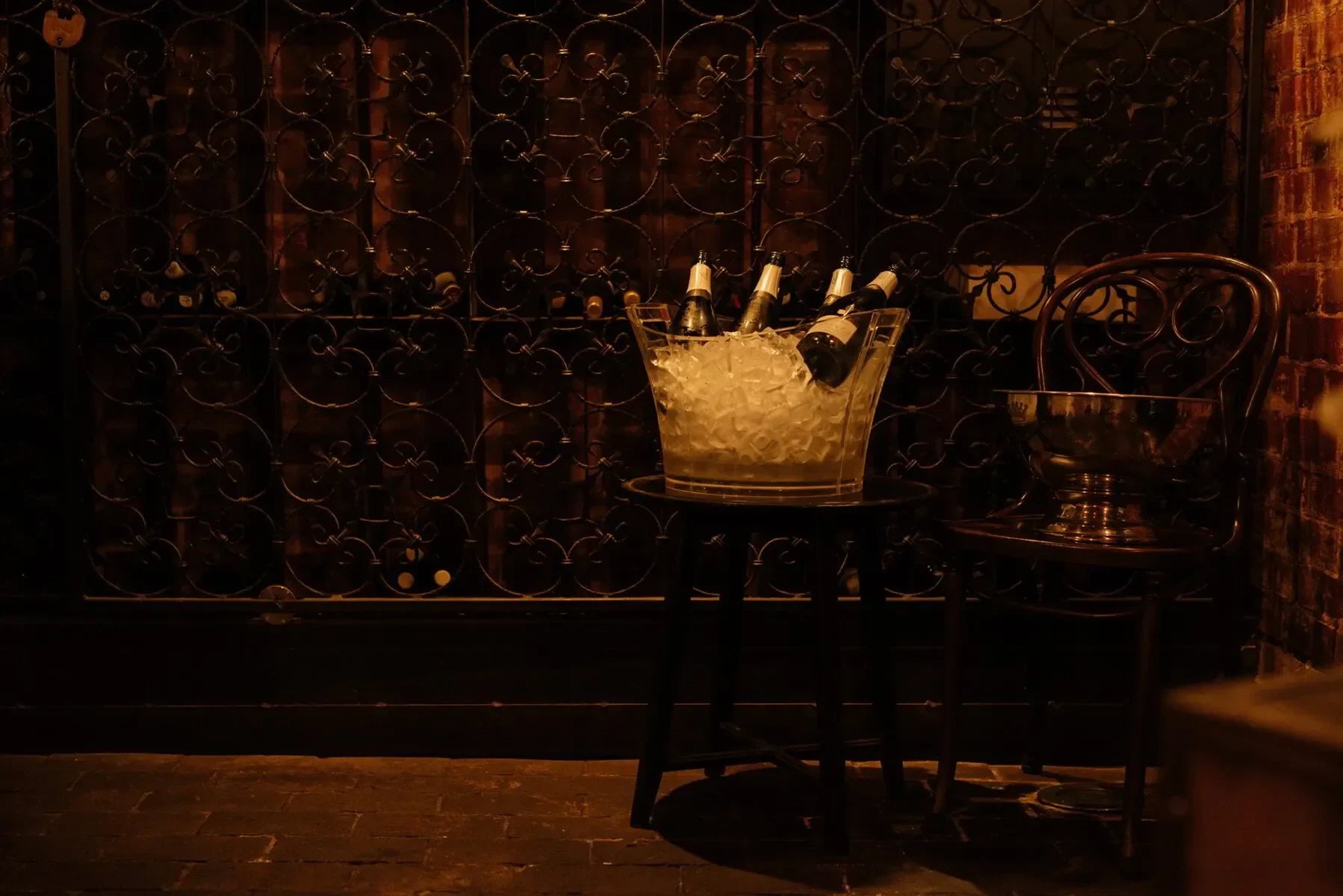 Champagne bottles in ice bucket on stool in dimly lit wine cellar with wrought iron gate