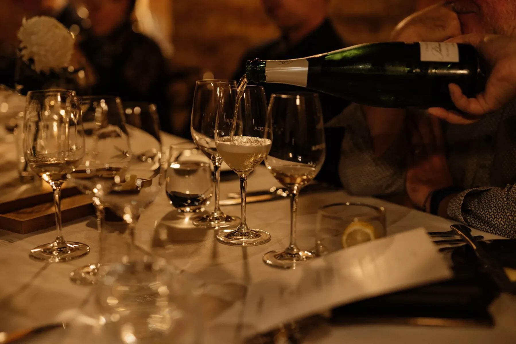 Champagne being poured into wine glass at elegant dinner table with candlelight ambiance