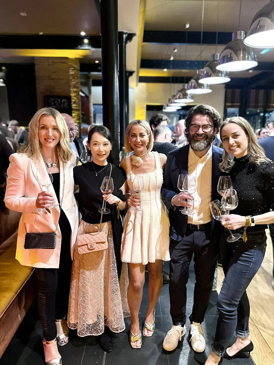 Group of five people dressed elegantly holding wine glasses at a modern indoor event