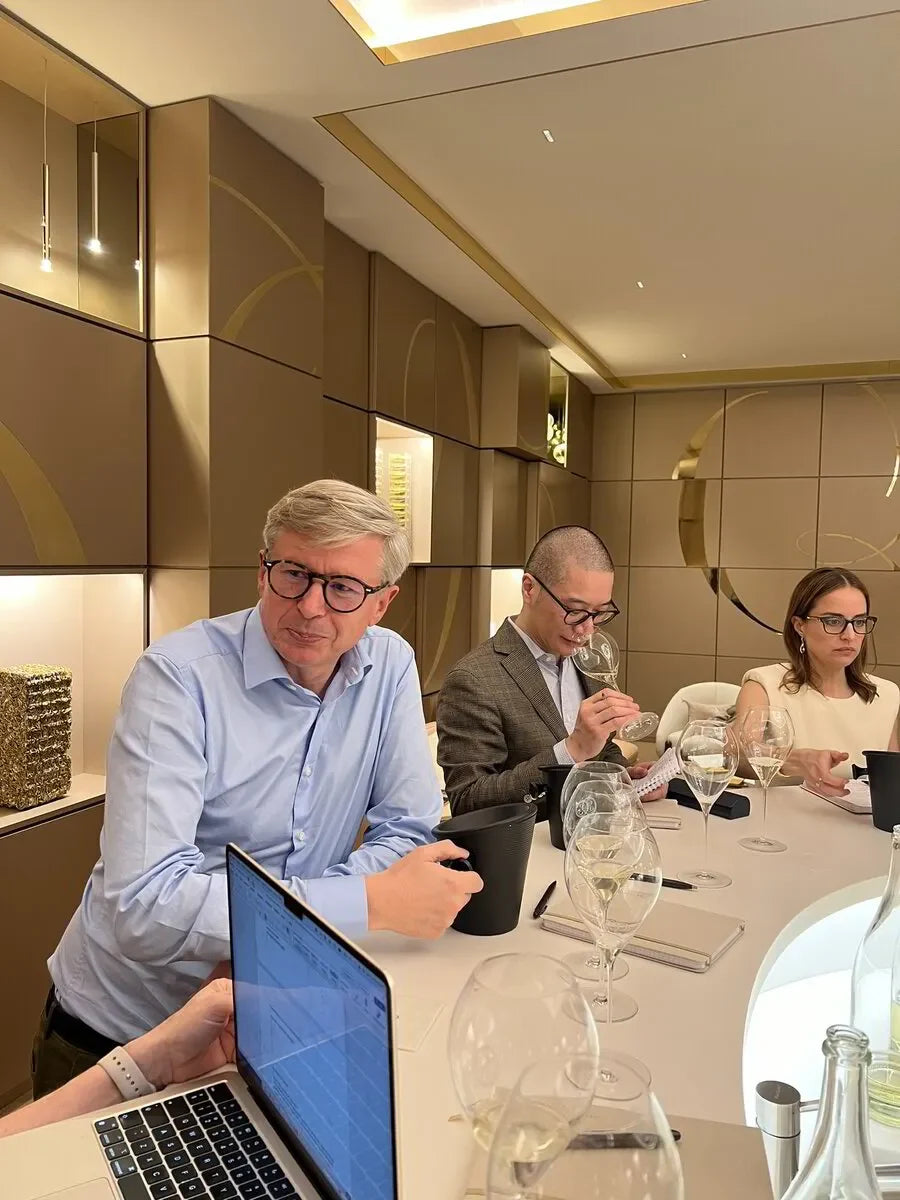 Three people wine tasting at a modern, elegant table with glasses and laptops