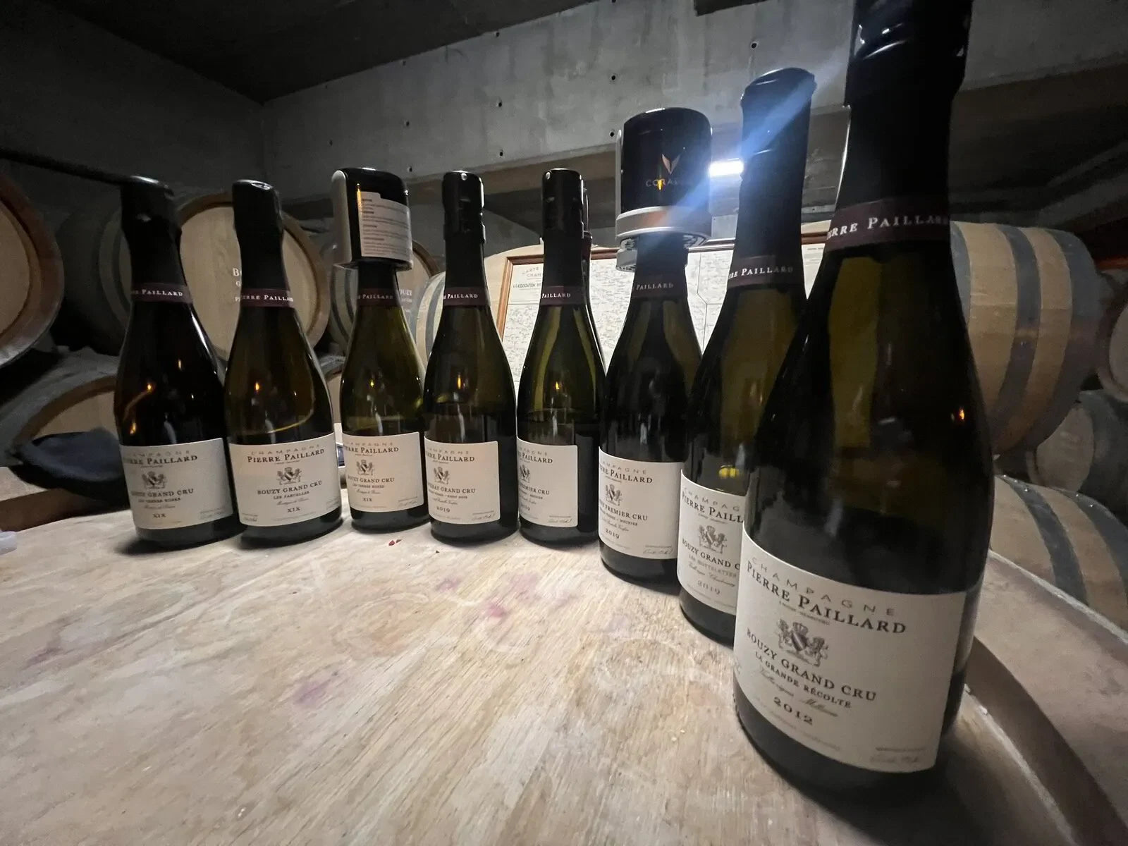 Pierre Paillard Champagne bottles arranged on a wooden table in a wine cellar with barrels