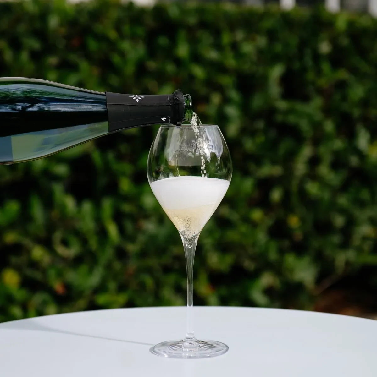 Champagne being poured into a Lehmann Jamesse glass on a white table outdoors