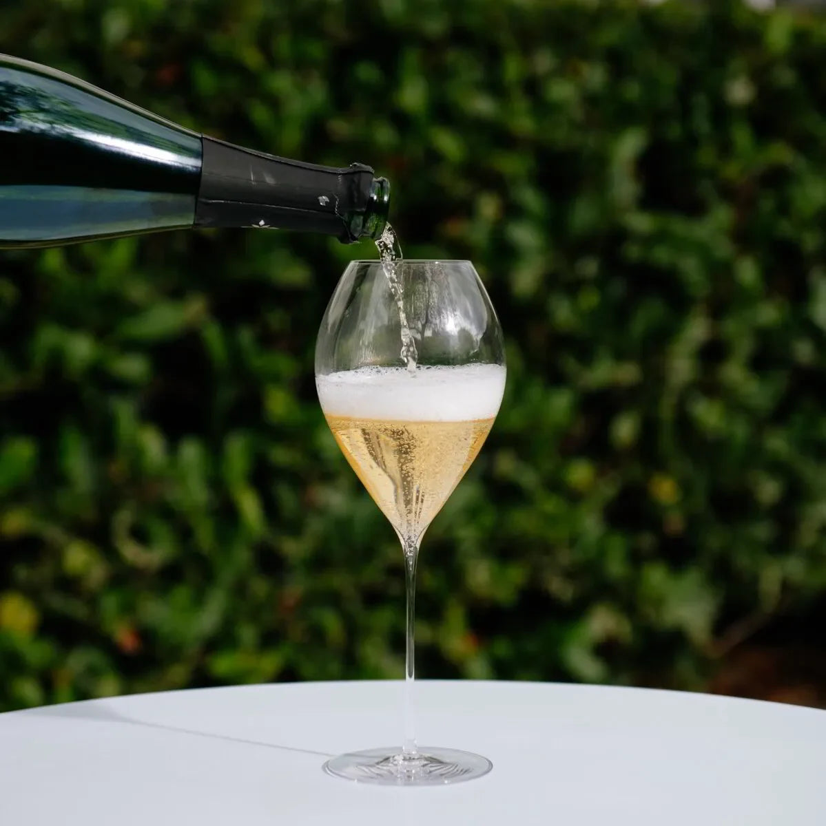 Champagne being poured into a tall flute glass on a white table outdoors