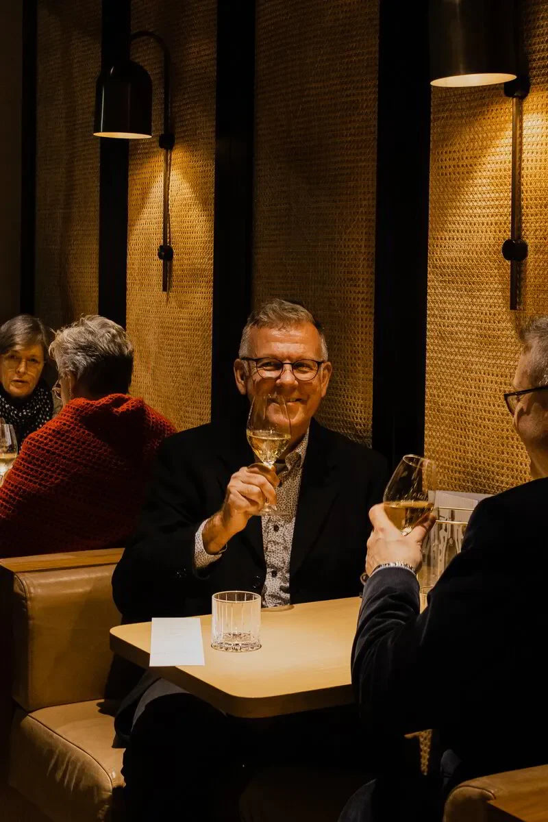 Two men toasting with wine glasses in a cozy restaurant booth with warm lighting.