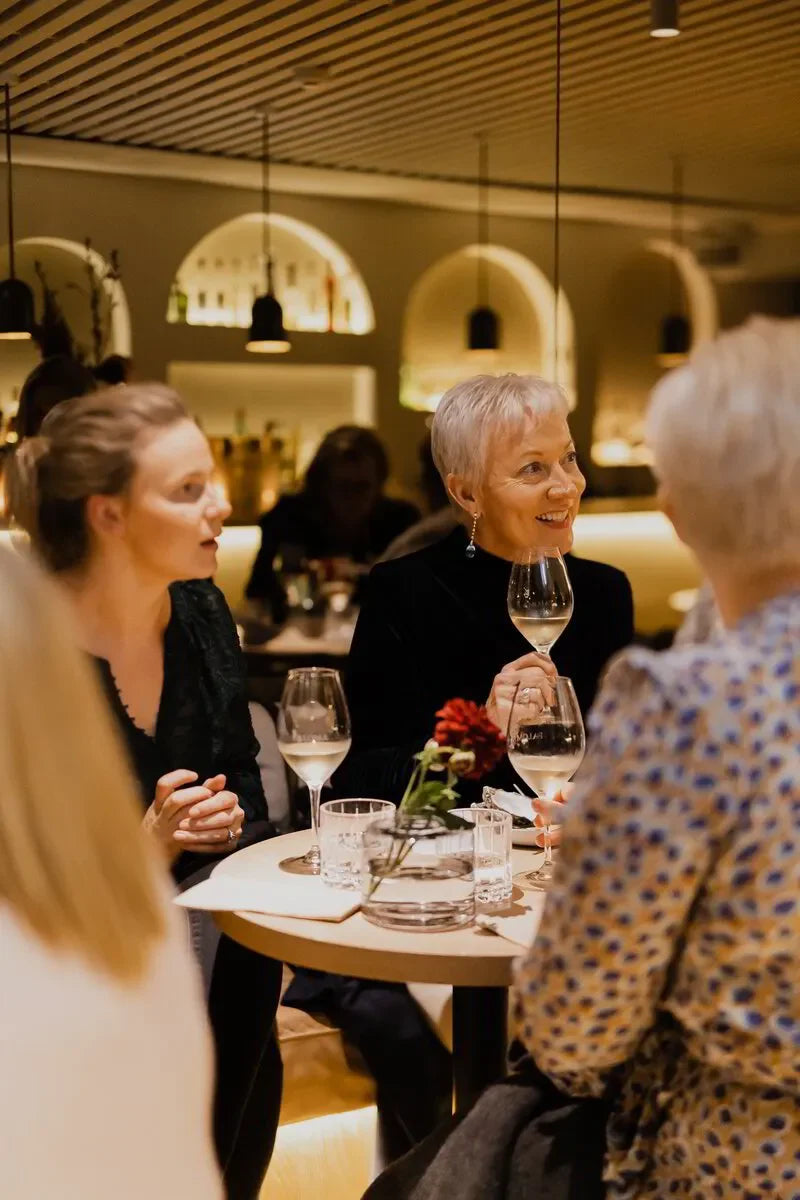 Women enjoying wine and conversation at a stylish, warmly lit restaurant table