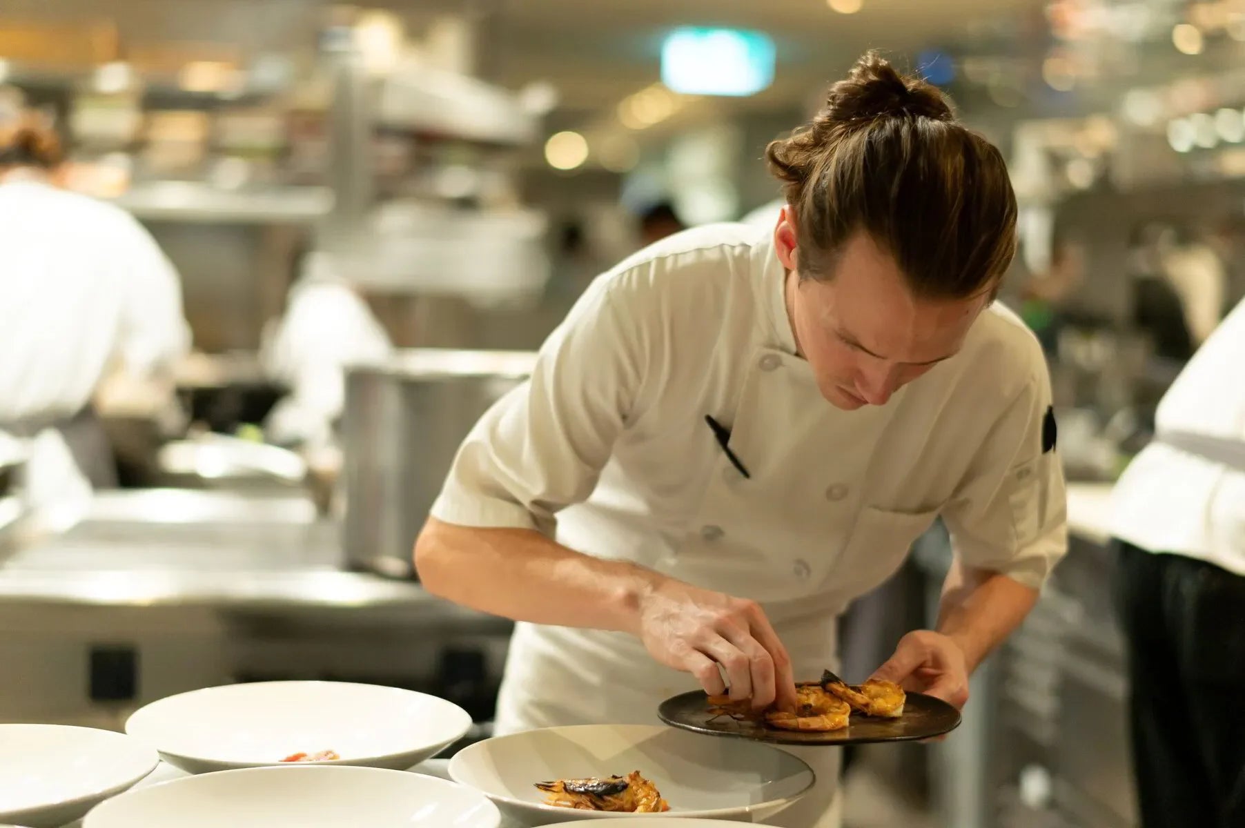 Chef plating gourmet food in a busy restaurant kitchen with white plates