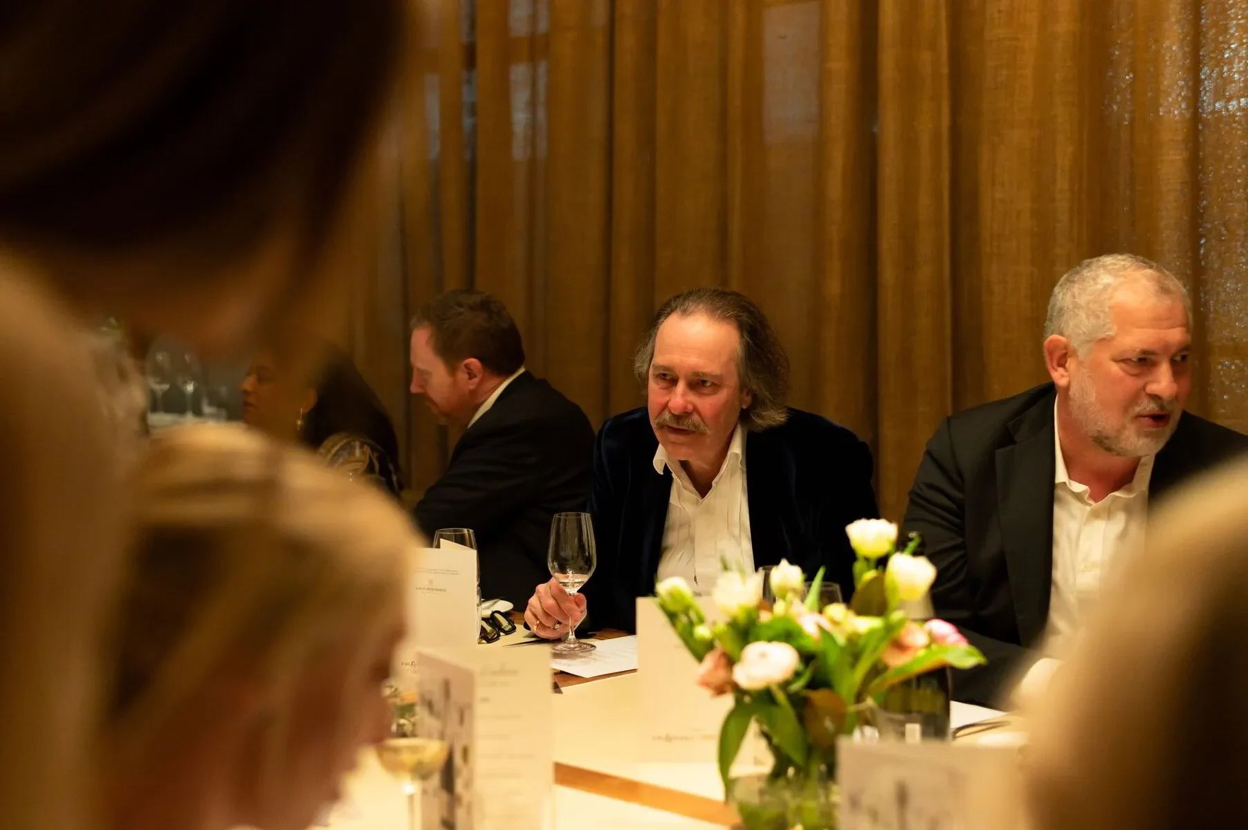 Elegant dinner party with men in suits, wine glasses, and floral centerpiece on table