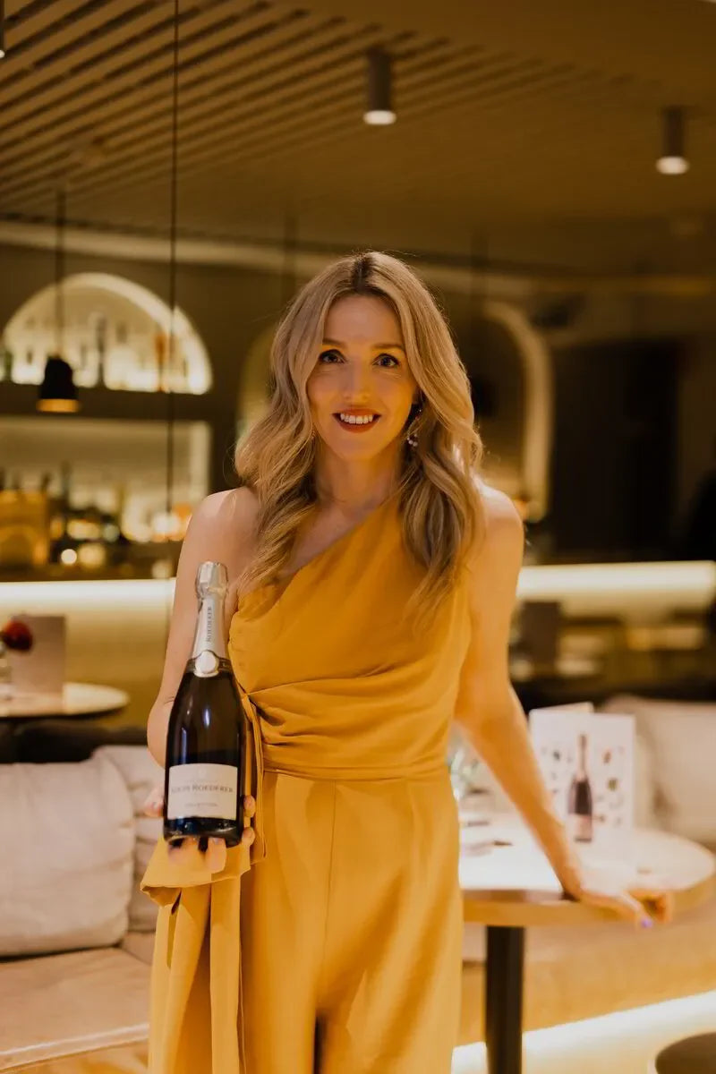 Woman in yellow dress holding Louis Roederer champagne bottle in elegant restaurant