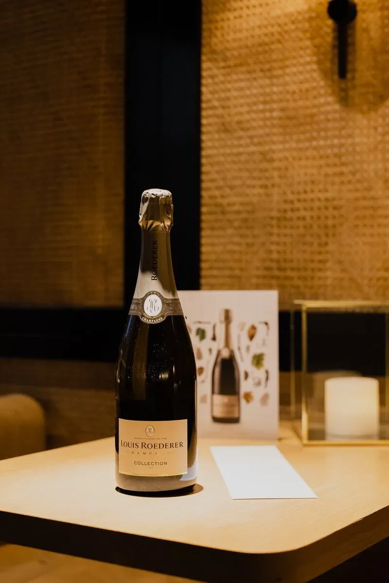 Louis Roederer Collection 242 champagne bottle on a wooden table in a cozy indoor setting