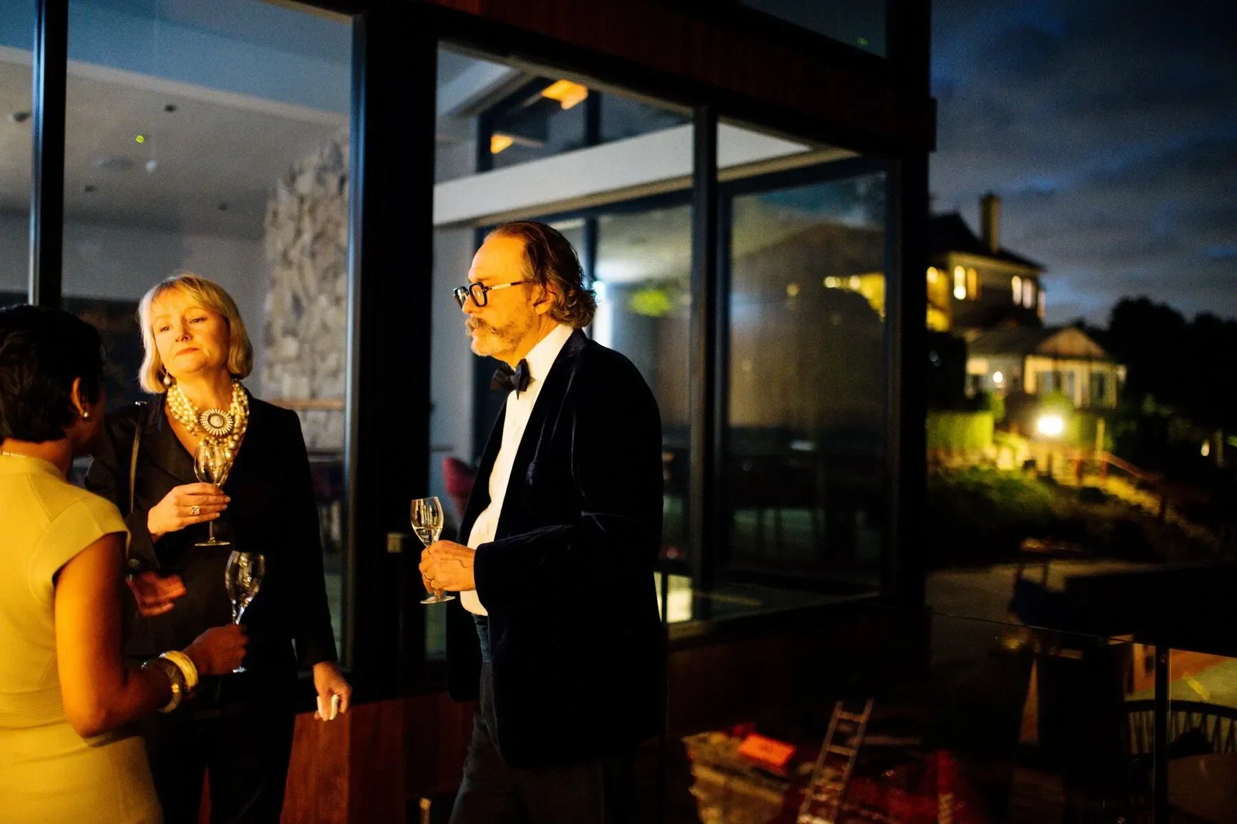Elegant adults in evening wear socializing at night with wine outside a modern house