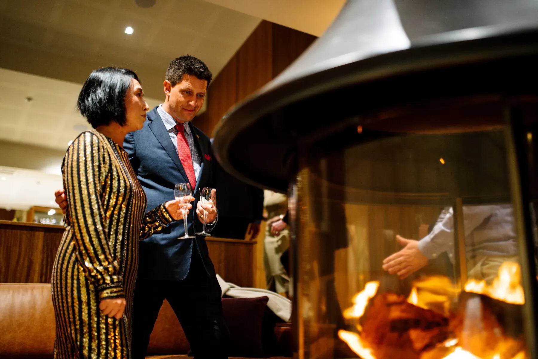 Elegant couple with champagne by indoor fireplace in upscale lounge setting