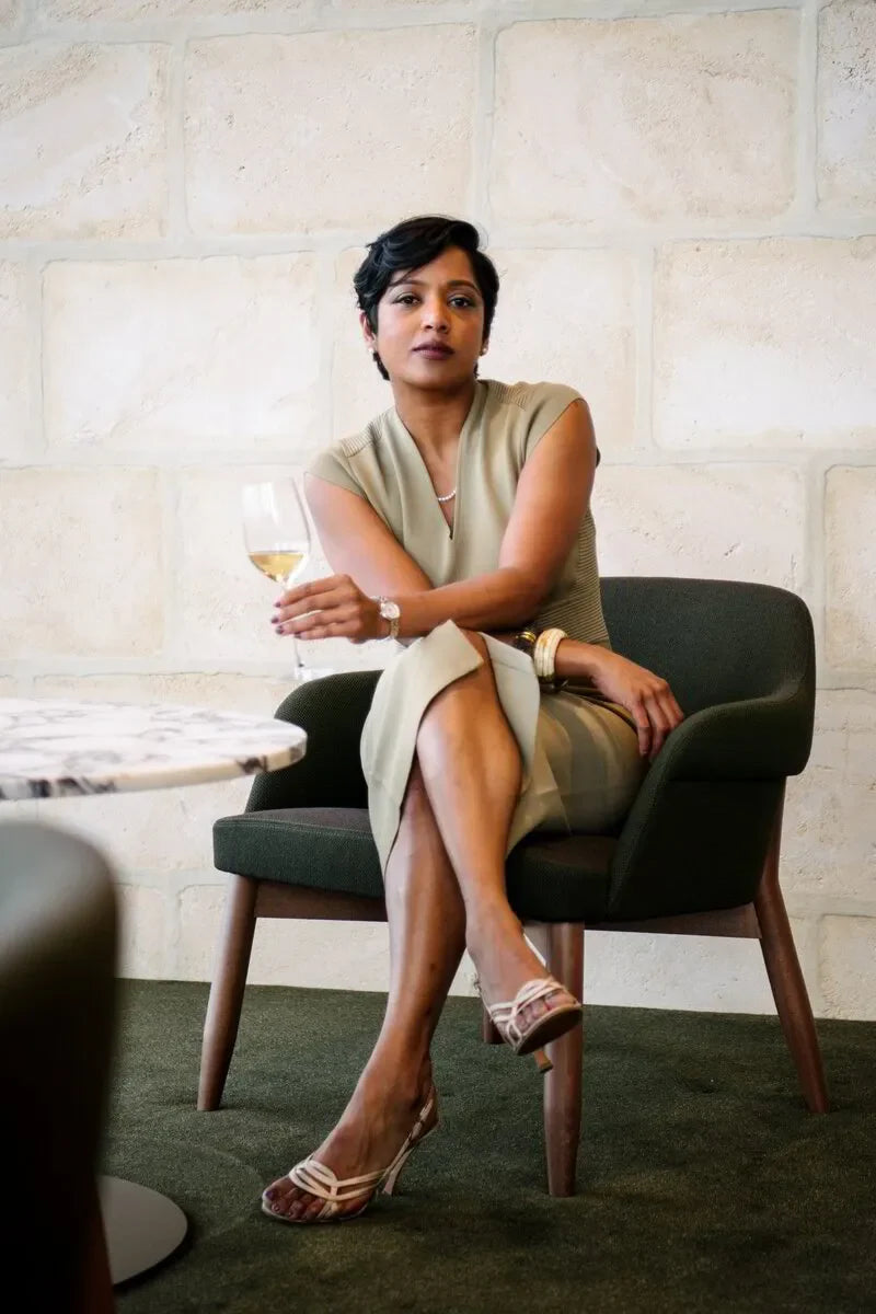 Woman in beige dress holding wine glass, seated on green chair by marble table, modern interior