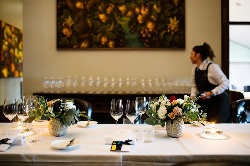 Elegant dining table with floral centerpieces, wine glasses, and a server in a formal restaurant.