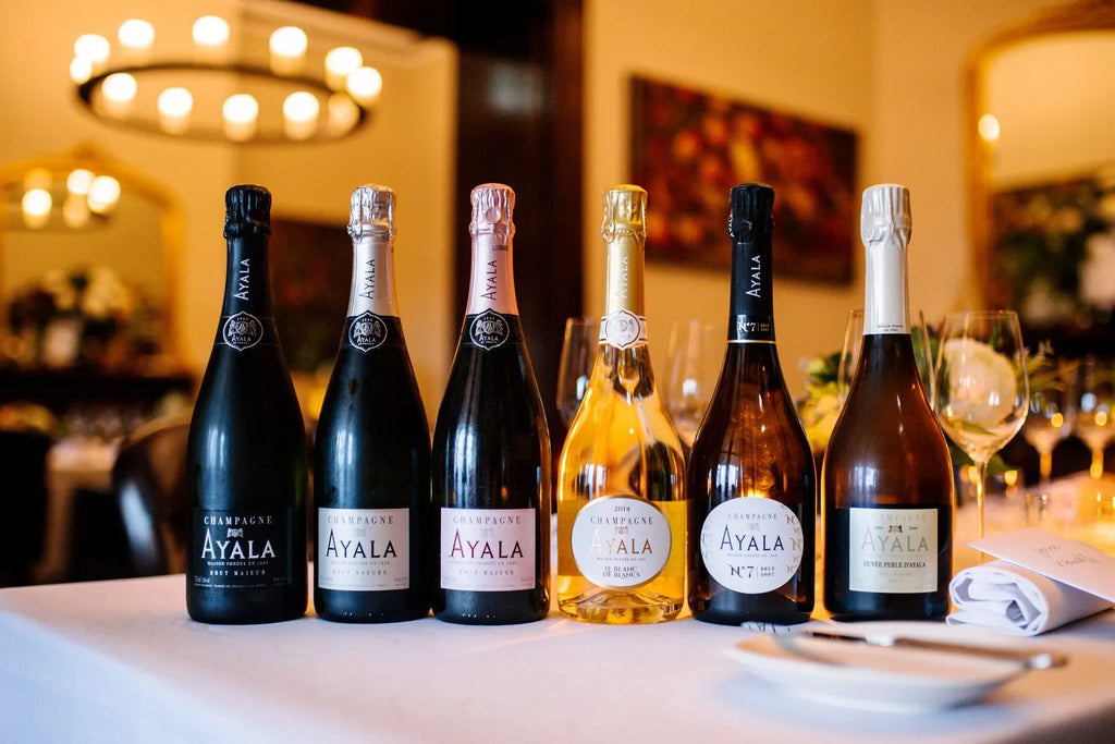 Six Ayala Champagne bottles lined up on a white tablecloth in an elegant dining room