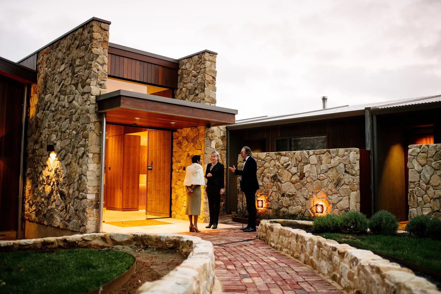 Modern stone house entrance with three people in formal attire at dusk