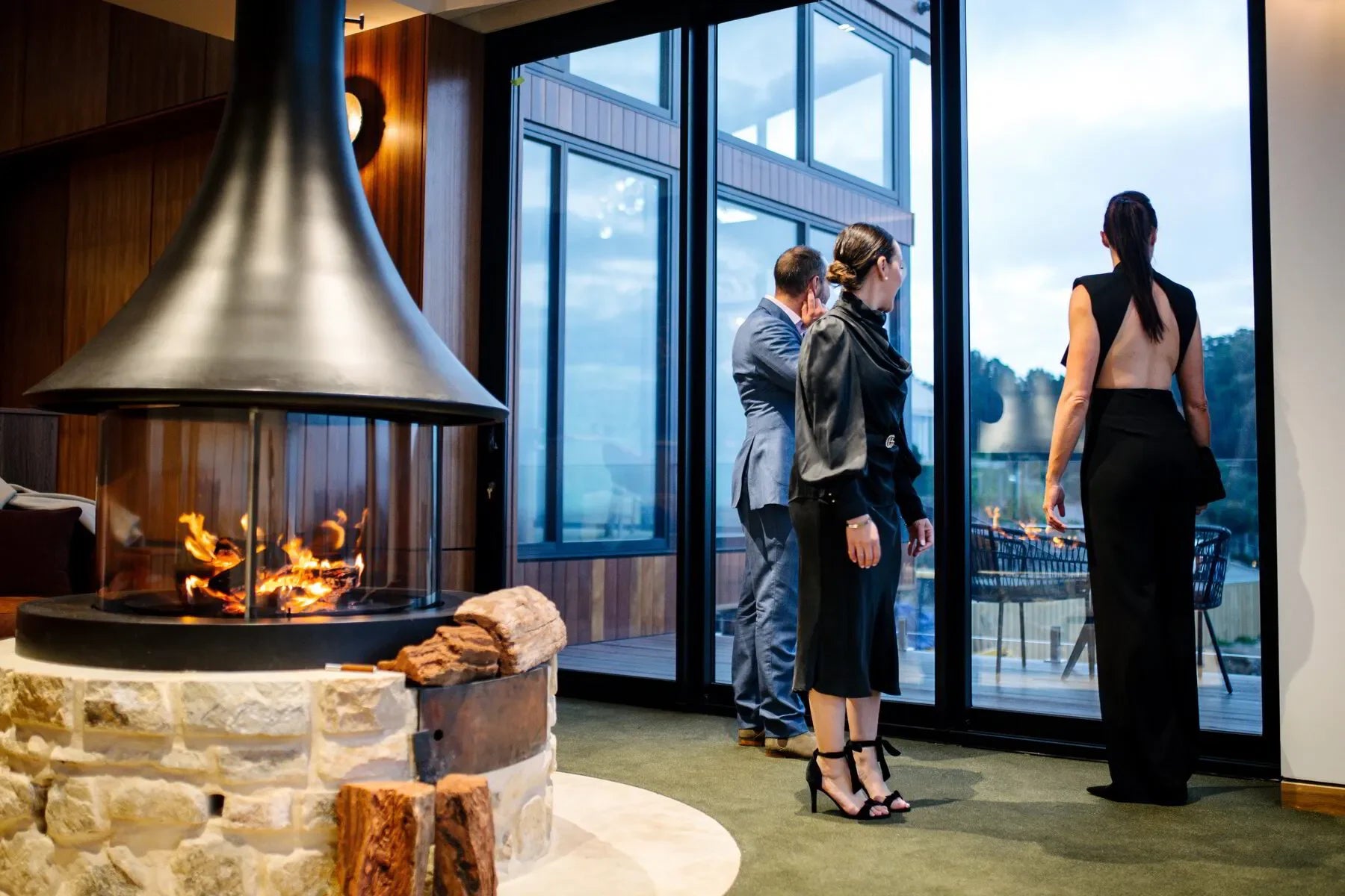 People in formal wear near modern indoor fireplace and large glass windows in luxury setting