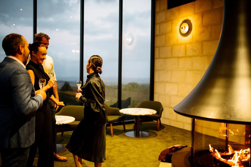 Group enjoying wine by modern fireplace in a cozy lounge with large windows and scenic view
