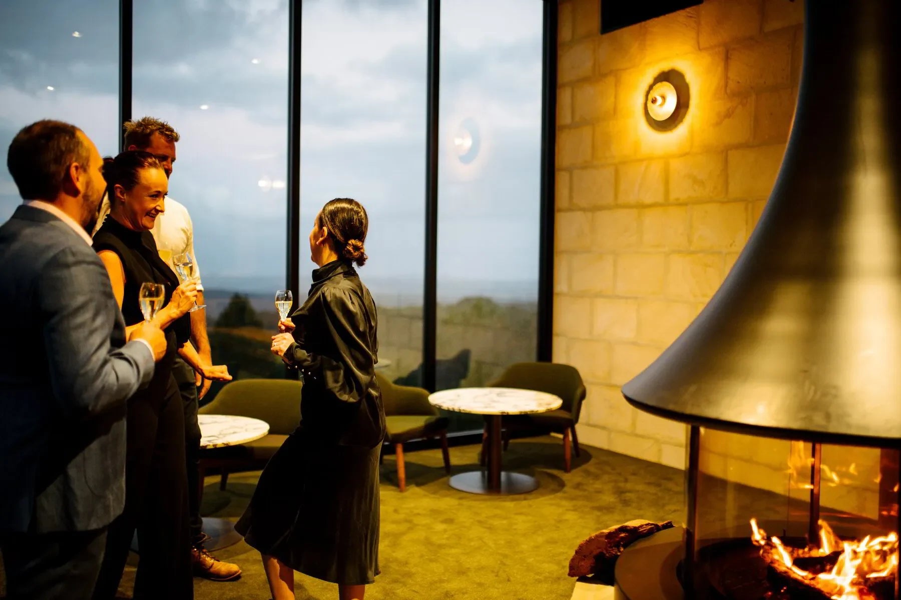 Group enjoying wine by modern fireplace in a cozy lounge with large windows and scenic view