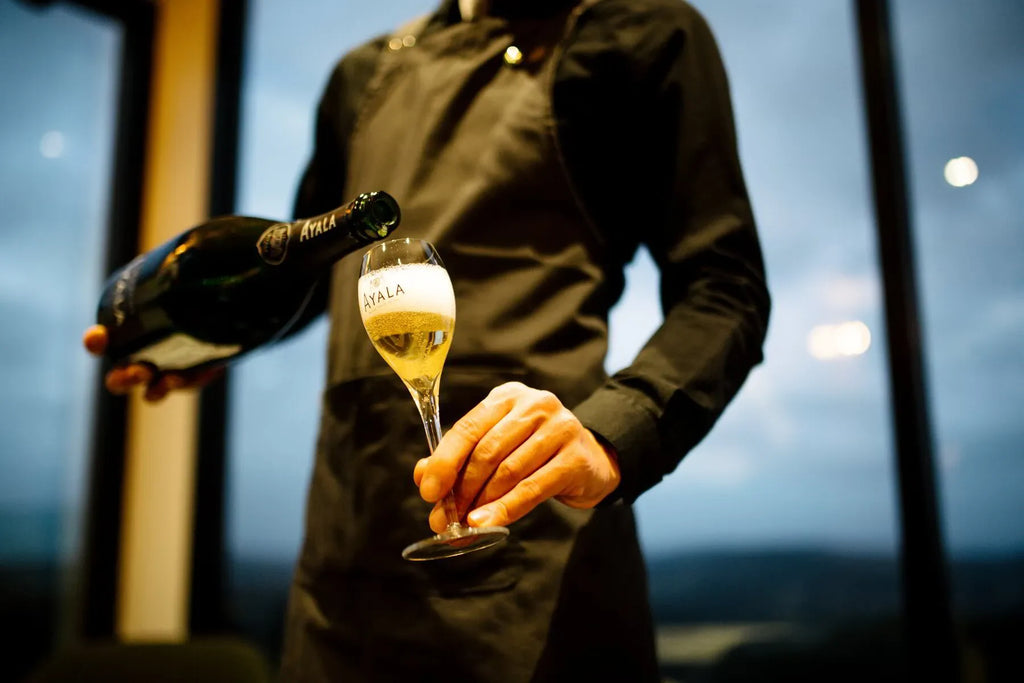 Waiter pouring Ayala champagne into glass in elegant indoor setting