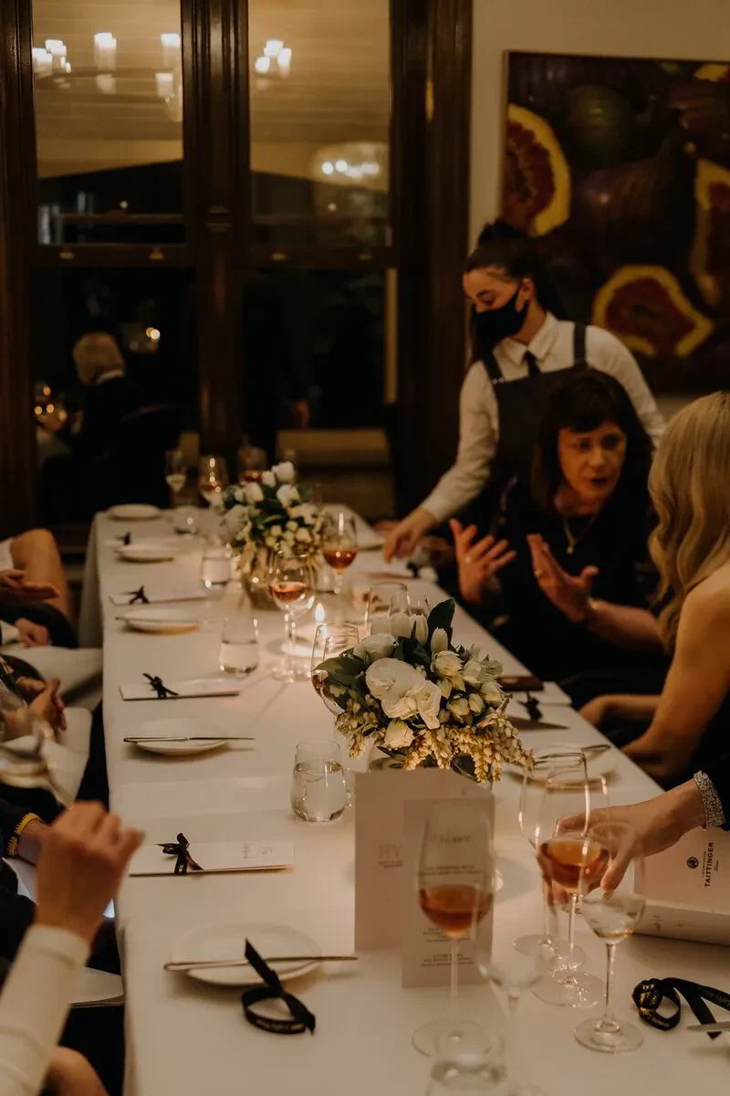 Elegant dinner party with wine glasses, white floral centerpieces, and guests at a long table