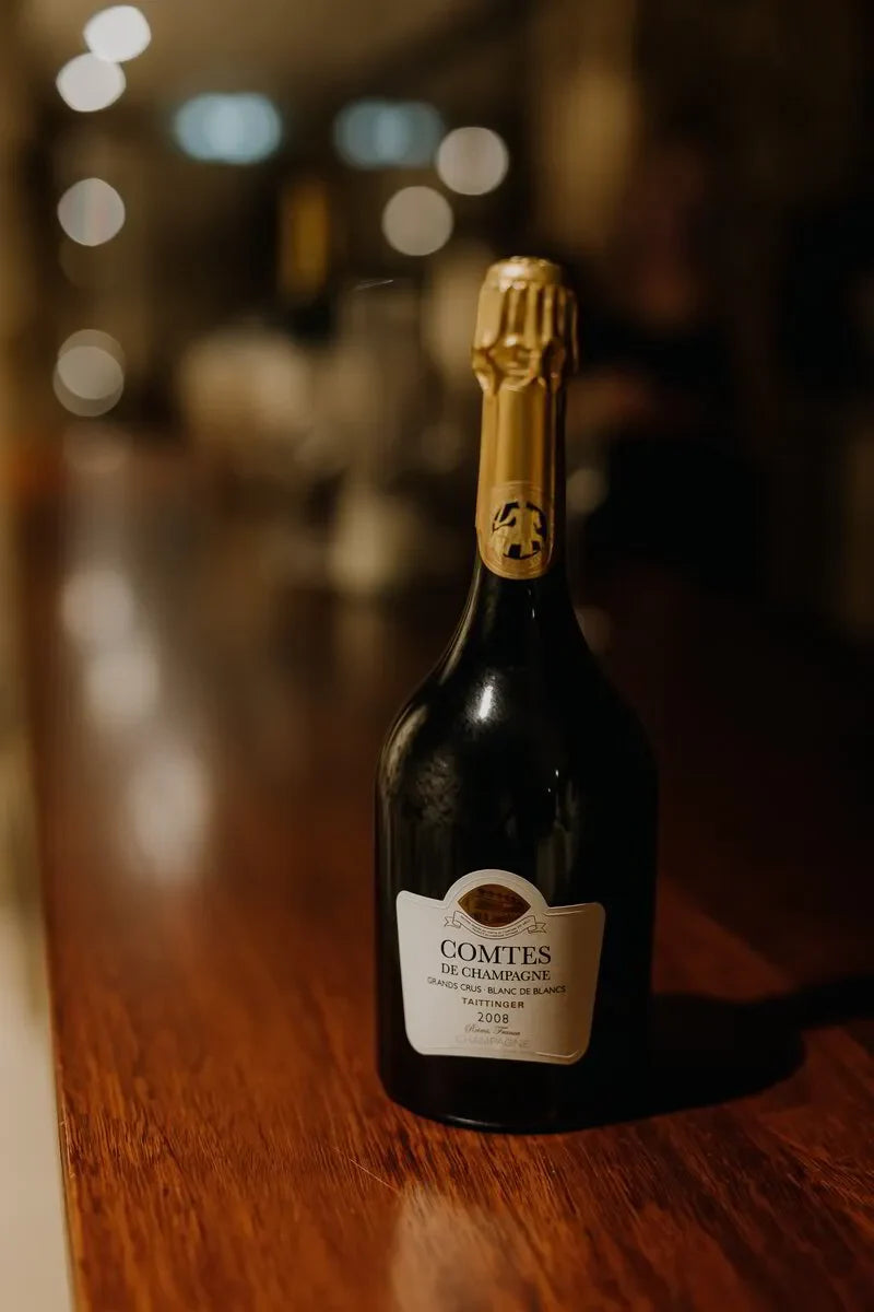 Taittinger Comtes de Champagne 2008 bottle on polished wooden bar in dim lighting