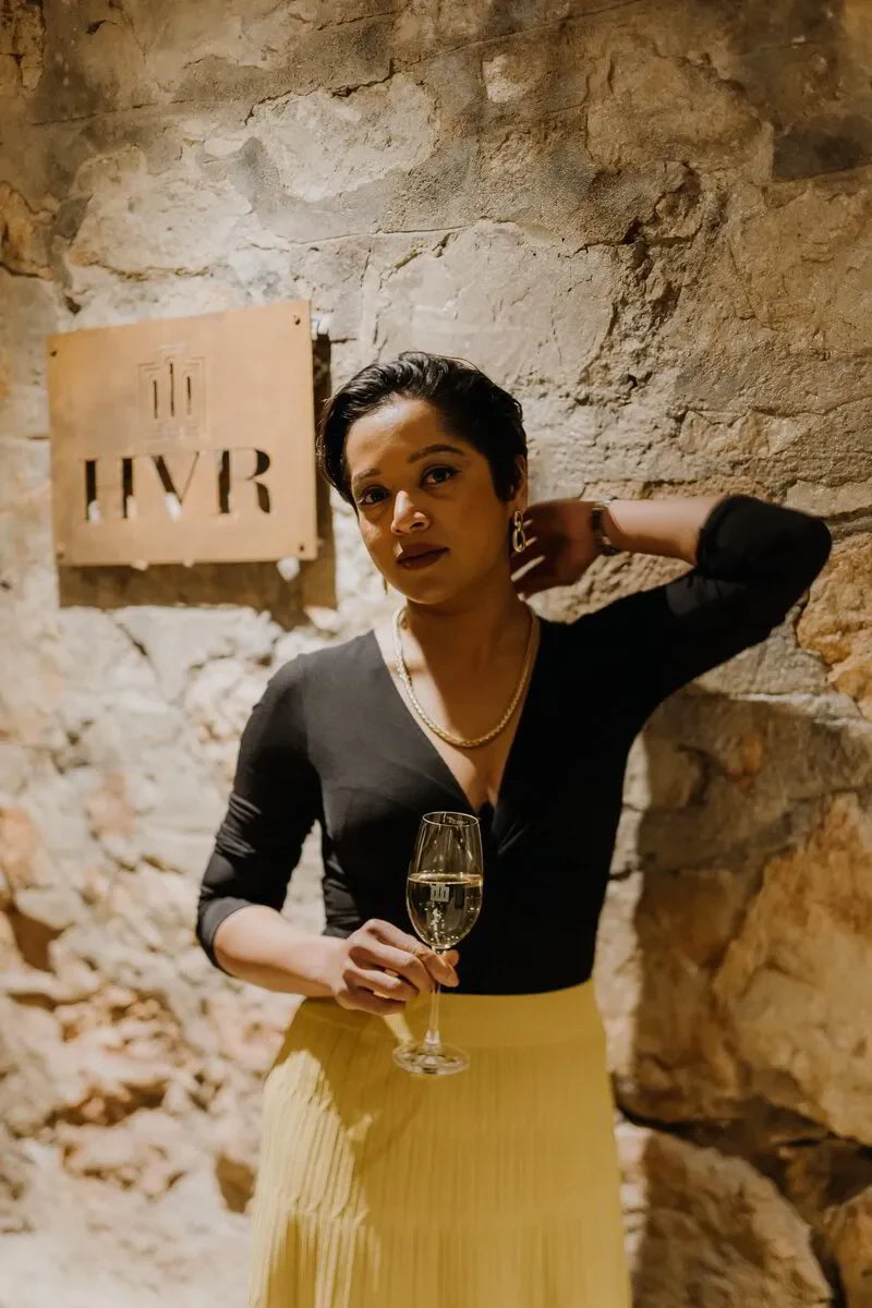 Woman holding wine glass in elegant attire at stone wall venue with HVR sign