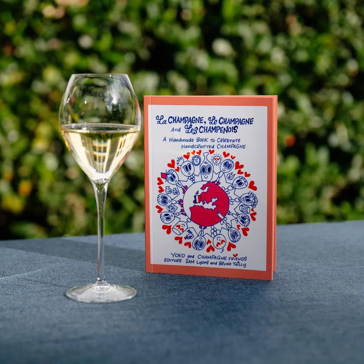 Glass of champagne next to 'La Champagne, Le Champagne et Les Champenois' book on blue table outdoors